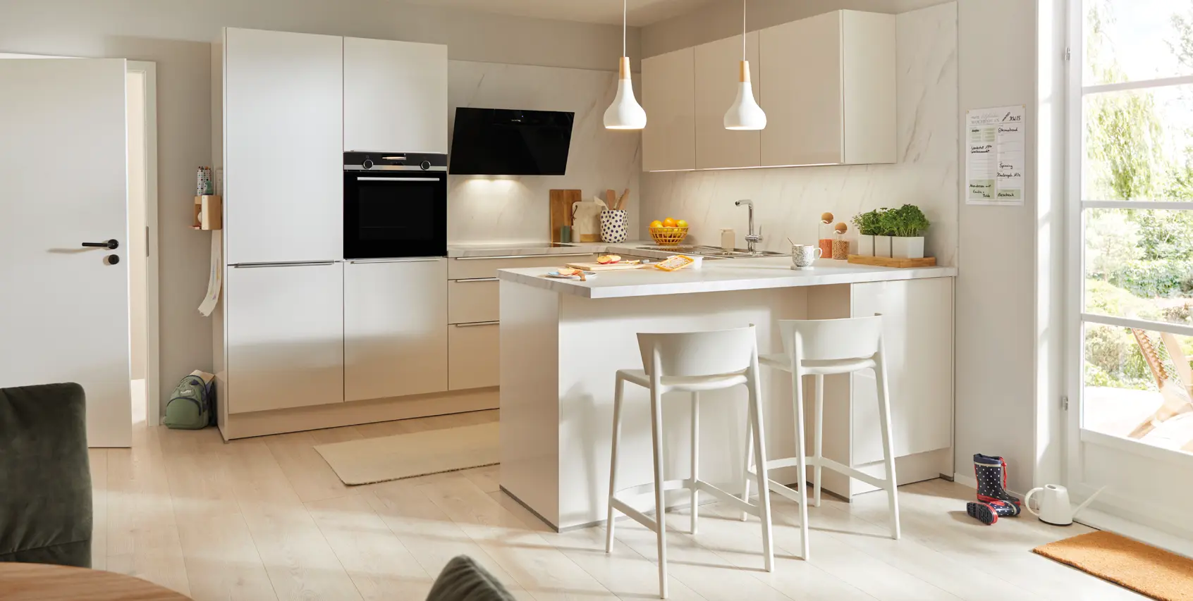 Helles WohnzimHelle moderne Küche in Weiß mit Kochinsel, Barhockern und integrierten Elektrogeräten. Klare Linien, viel Tageslicht und hochwertige Materialien zeigen zeitloses Küchendesign für offene Wohnkonzepte.mer mit modernem Ecksofa in Beige, großem Teppich und Couchtisch. Freundliche Einrichtung mit Pflanzen, Tageslicht und ruhigen Farben für ein gemütliches und stilvolles Wohnen.